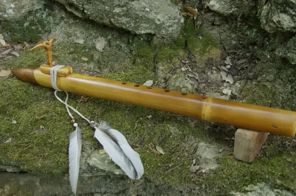 Flûte en bambou, ornée d'un oiseau sculpté et de plumes, prête à fabriquer des mélodies naturelles.
