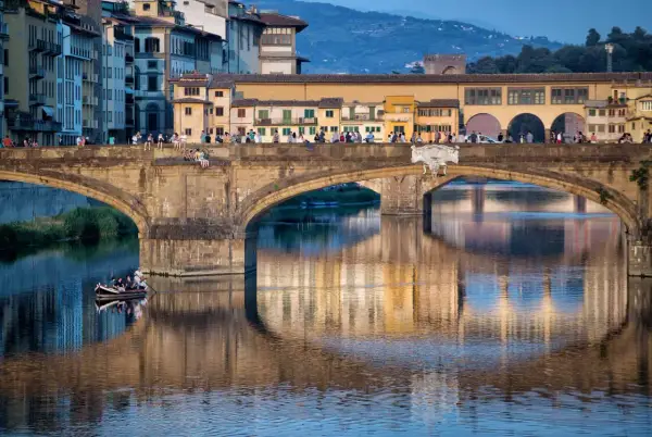 Le Ponte Vecchio à Florence, avec ses maisons colorées et ses reflets sur l'Arno. Une barque navigue paisiblement sous le pont.