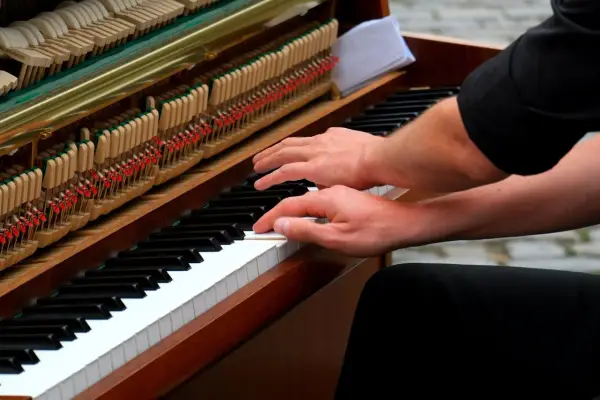 Mains sur le clavier d'un piano, prêt à jouer d'un instrument. Les marteaux et les cordes sont visibles.