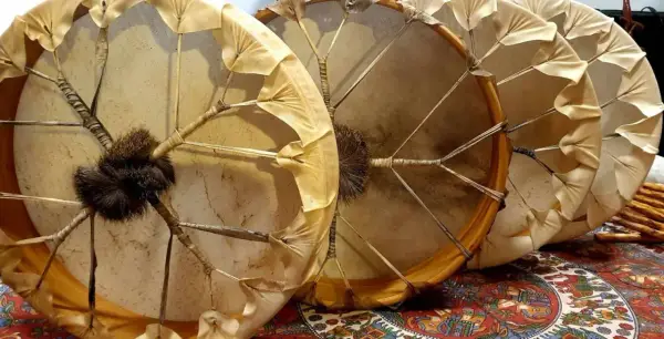 Trois tambours chamaniques, un instrument traditionnel aux peaux tendues et ornées de franges, prêts pour une cérémonie.